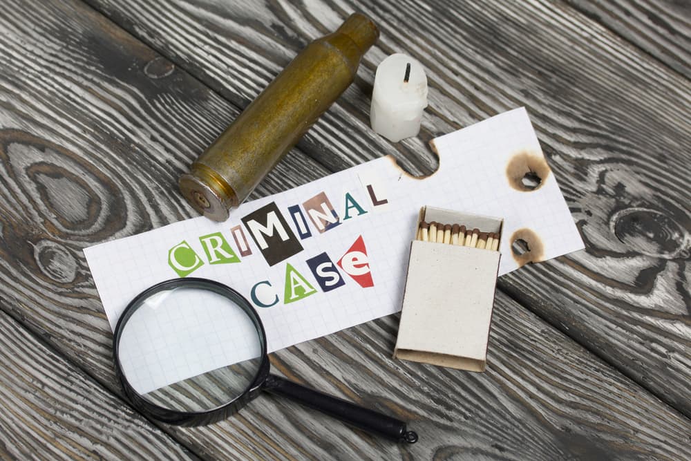Criminal case" spelled out with magazine letters, a spent cartridge, a magnifying glass, a candle stub, and matches nearby.