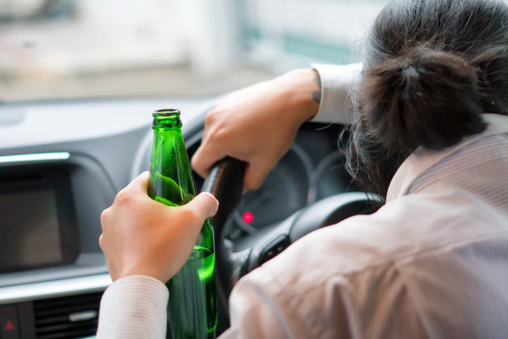 Man holding a bottle of beer while driving a car. Illustrates the dangers of drinking and driving. DUI and DWI concept.