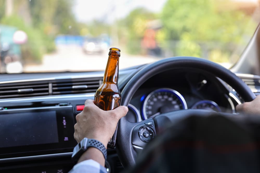 Man driving with alcohol bottle in hand - dangerous and illegal behavior that can lead to accidents.