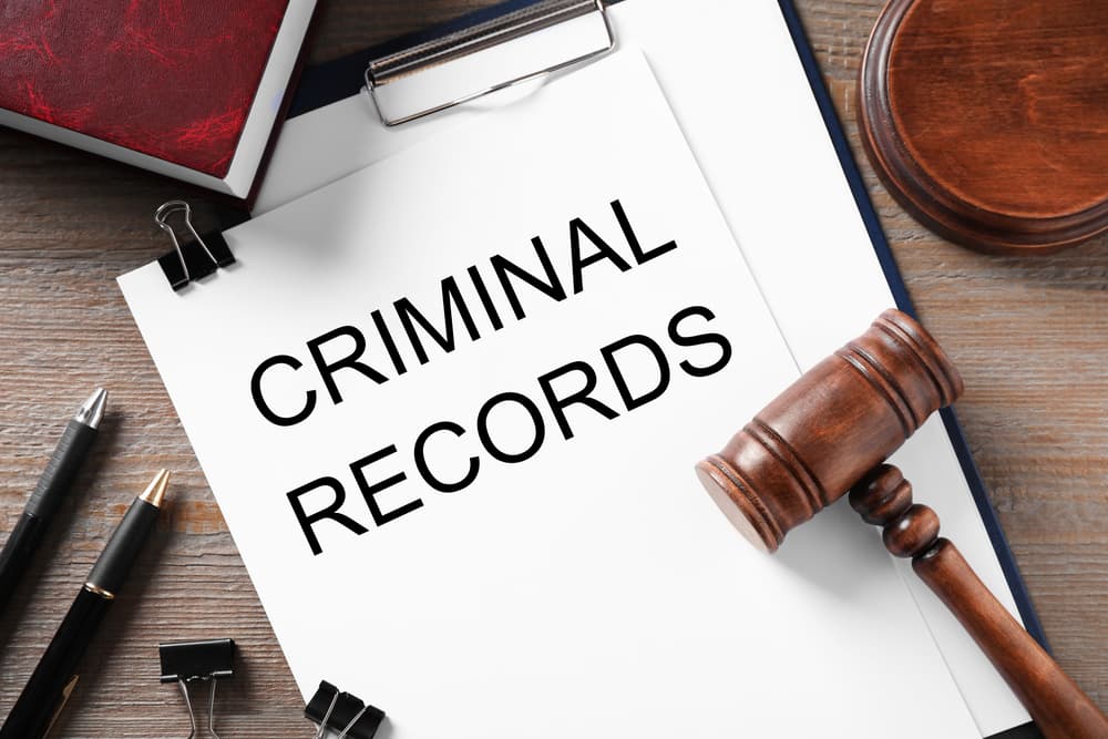 A clipboard with the words "CRIMINAL RECORD" alongside a gavel, both placed on a wooden table in a flat lay composition.