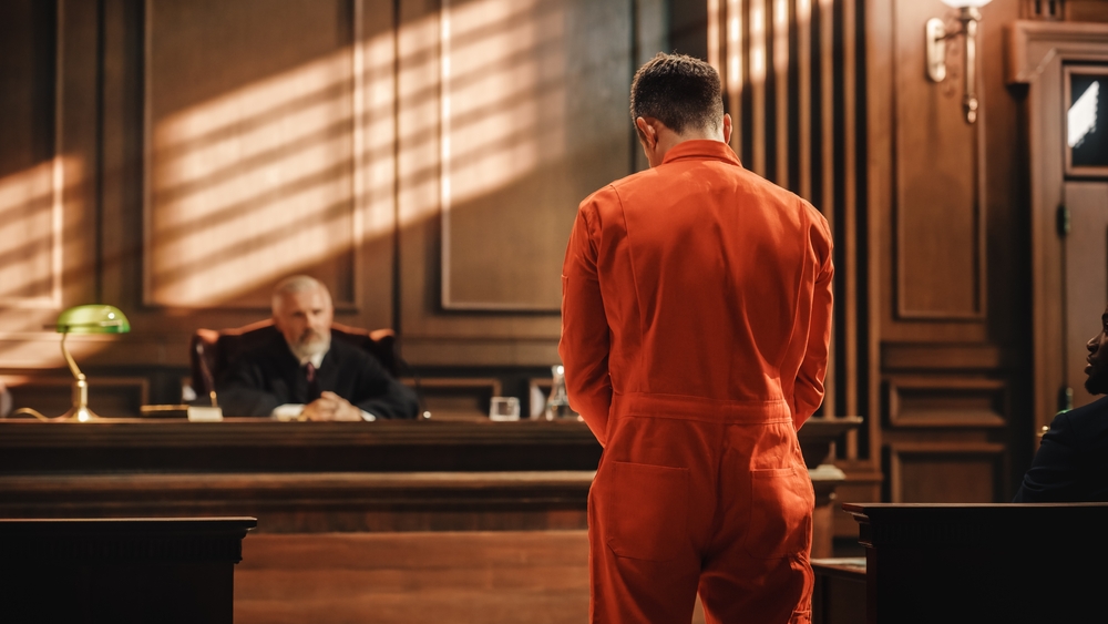 In a courtroom, a defendant in an orange jumpsuit is being questioned and giving testimony before the judge and jury, while denying the charges.