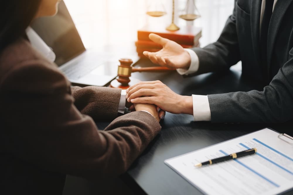 Lawyer holding hands and discussing contract papers with laptop and tabletat office room.