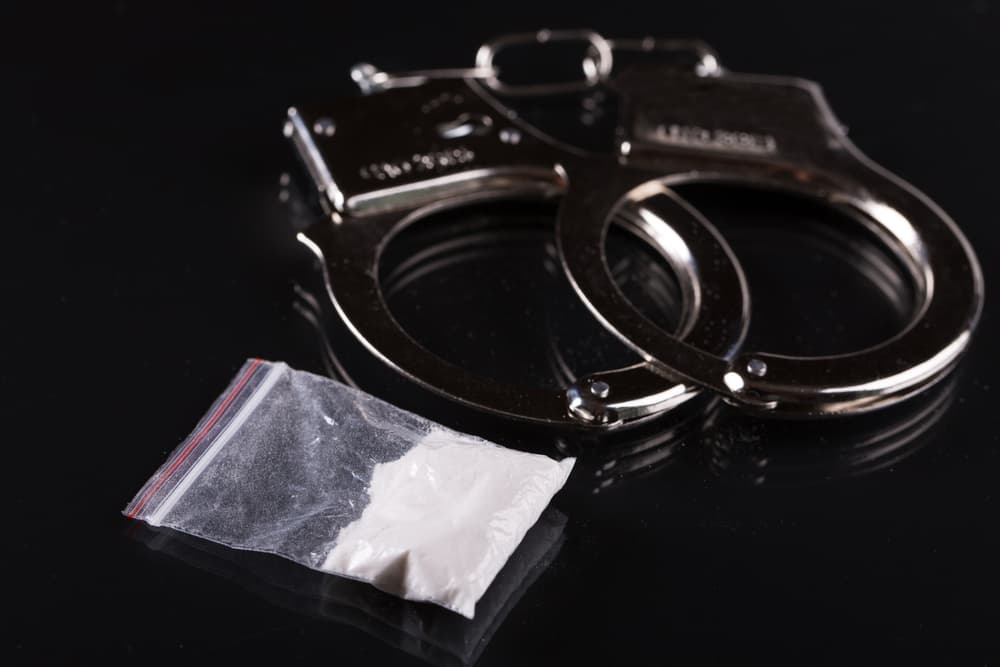 Handcuffs and cocaine on black background.