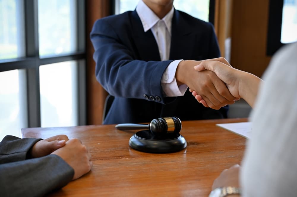 A professional male lawyer in a formal suit shakes hands with his client after making the deal and being hired to manage his lawsuit. 