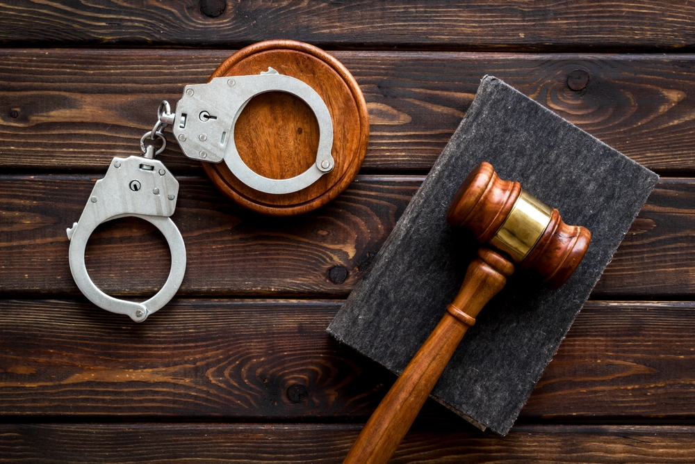 A pair of metal handcuffs placed beside a judge's gavel and a criminal code book, symbolizing criminal law and justice.