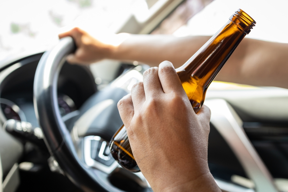 A drunk driver holding a beer bottle—an Asian male drinking alcohol while operating a vehicle—illustrates the risk and danger of road accidents. Don’t drink and drive.