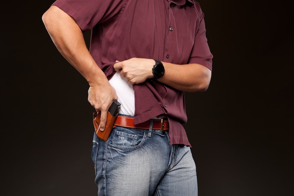 Man lifts shirt to reveal a concealed carry pistol draw from holster on belt.