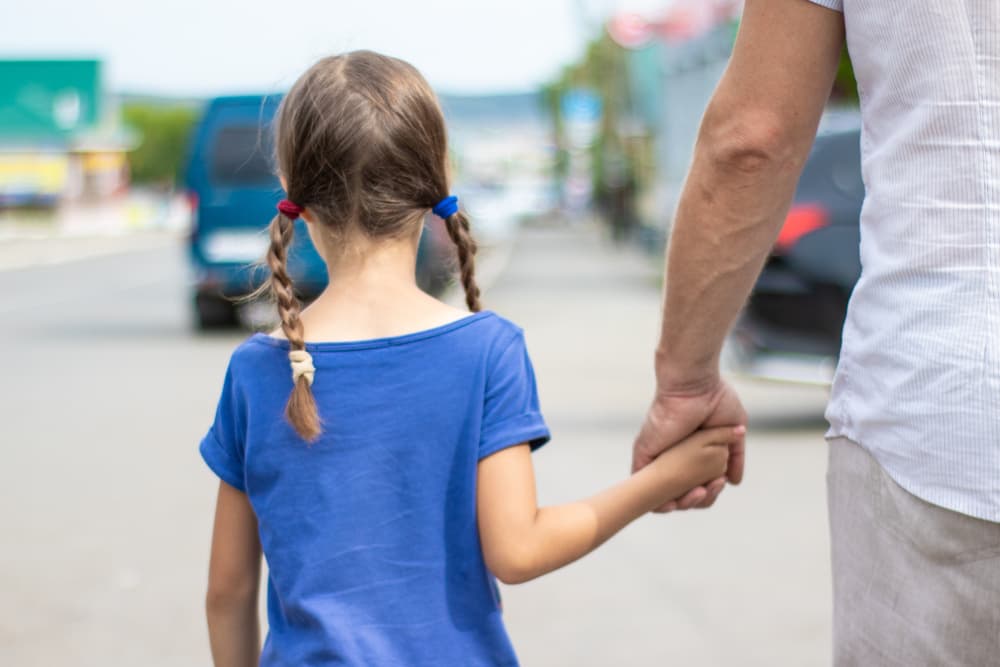 A man in white clothes leads a little girl by the hand along the street