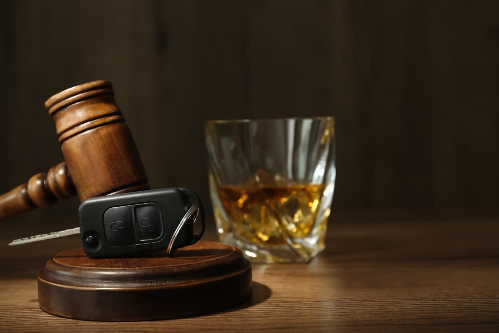 A car key and gavel placed beside a glass of alcohol on a wooden table, emphasizing the dangers of drinking and driving. Space available for text.