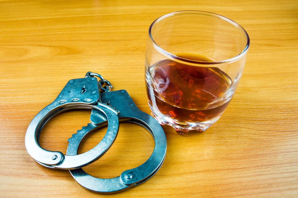 Close-up of handcuffs and a glass of whiskey on the table.