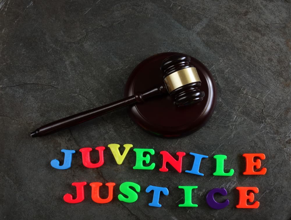 Colorful play letters spell out "Juvenile Justice" on a surface, with a gavel placed nearby. The playful letters contrast with the seriousness of the gavel, symbolizing the intersection of youth and the legal system, as well as the focus on rehabilitation in juvenile justice.