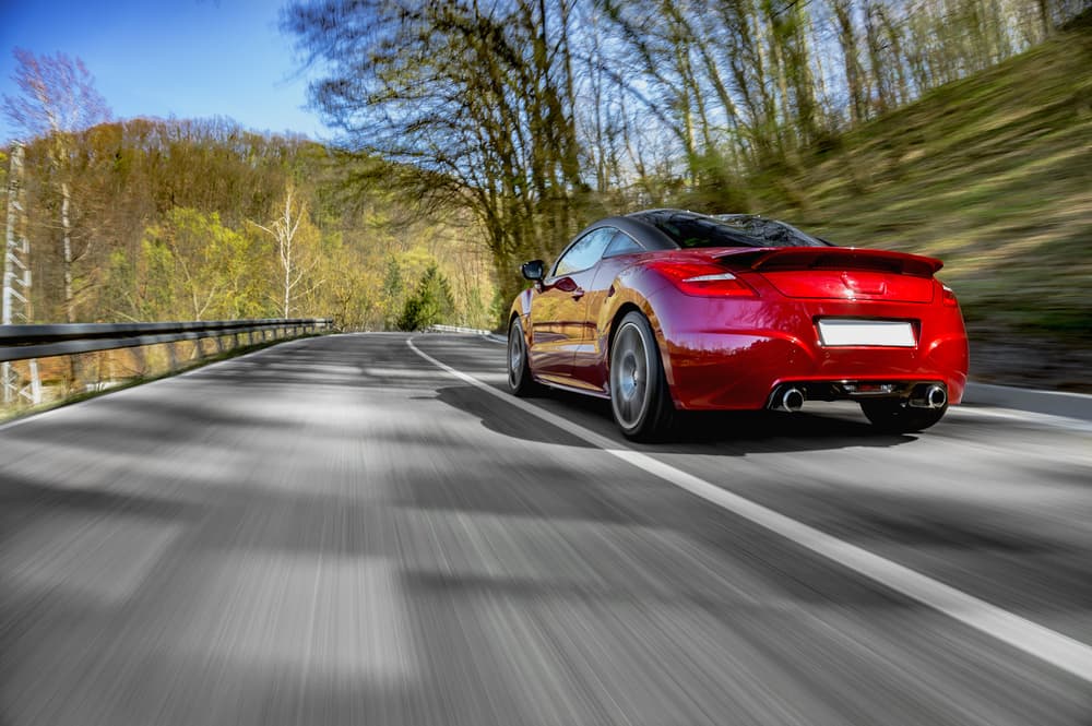 A sleek, generic red sports car speeding down an open road, with blurred motion effects to emphasize its high velocity.