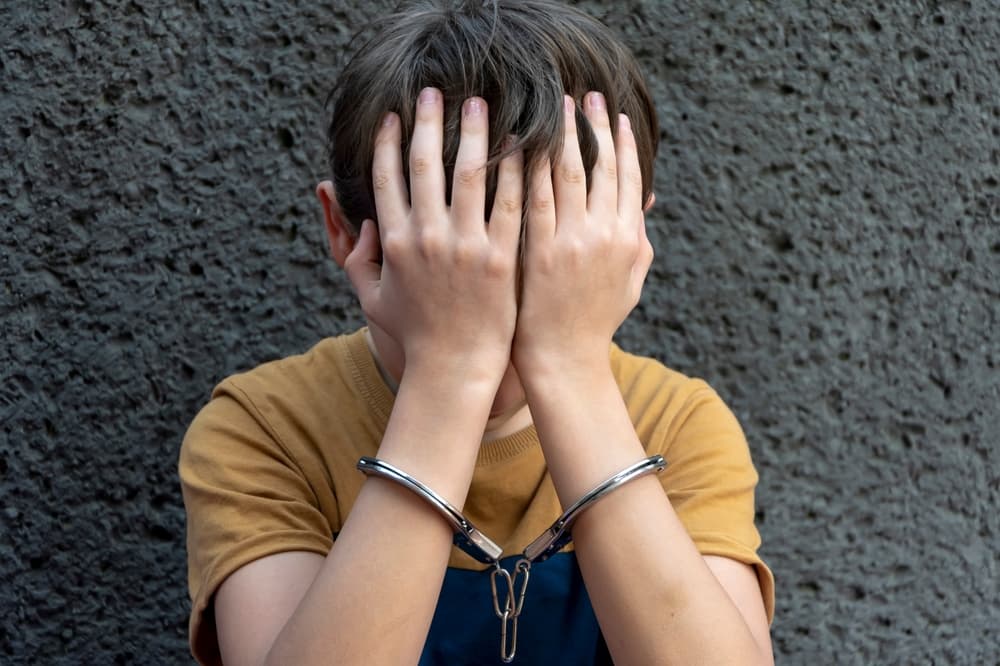 A 10-year-old boy, wearing handcuffs, sits against a gray background, symbolizing juvenile delinquency and the criminal liability of minors. 