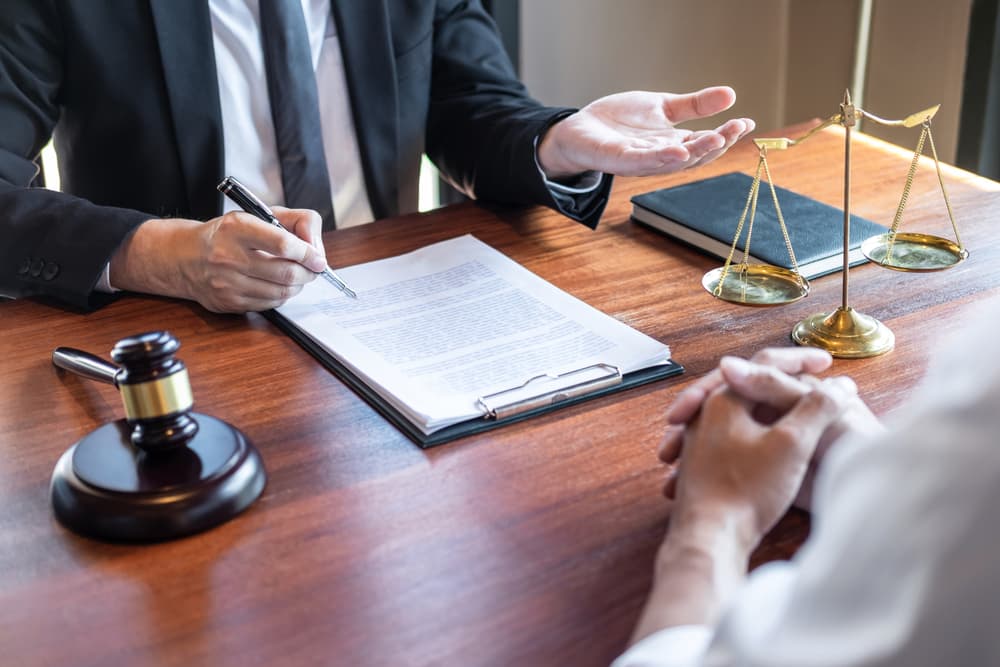 A male lawyer consulting with a client about a legal case negotiation in a courtroom, reviewing documents related to the case. 