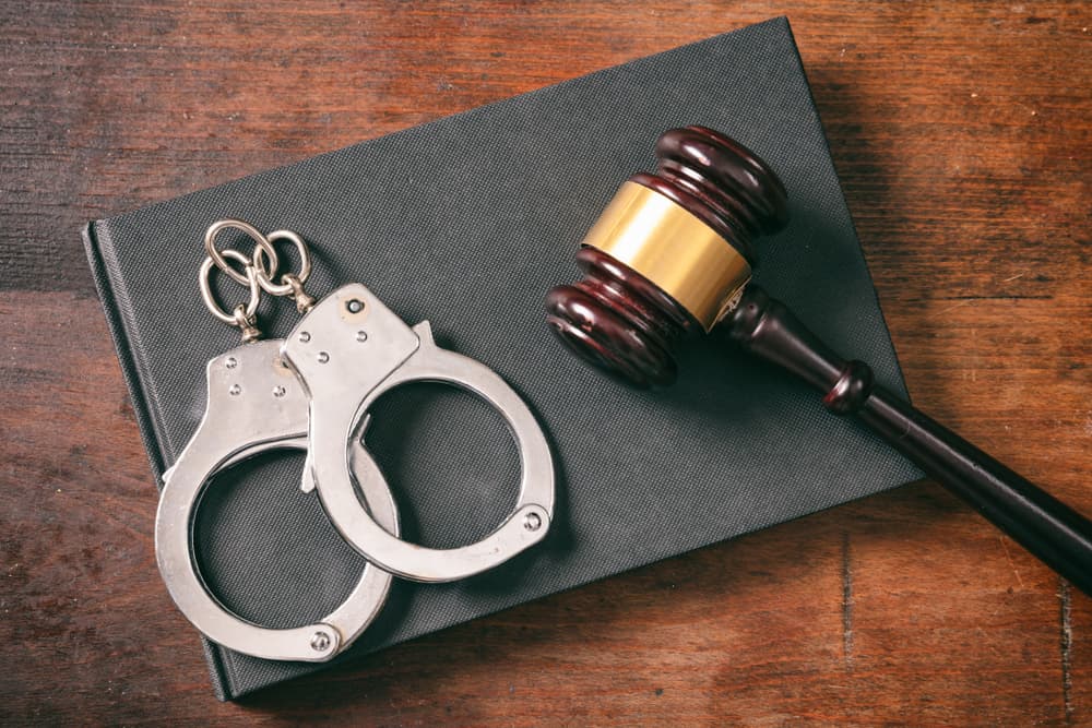 A top view of a wooden background featuring handcuffs and a gavel resting on a law book, symbolizing the concepts of law and order.