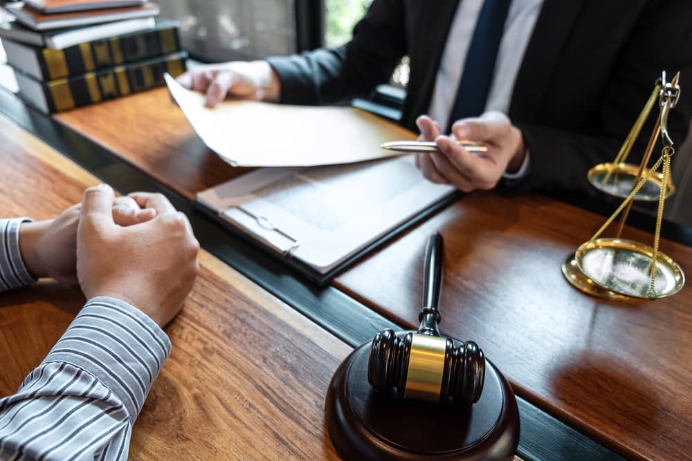 A male lawyer is discussing a legal case negotiation with a client in a courtroom, surrounded by legal documents, emphasizing law and justice concepts.






