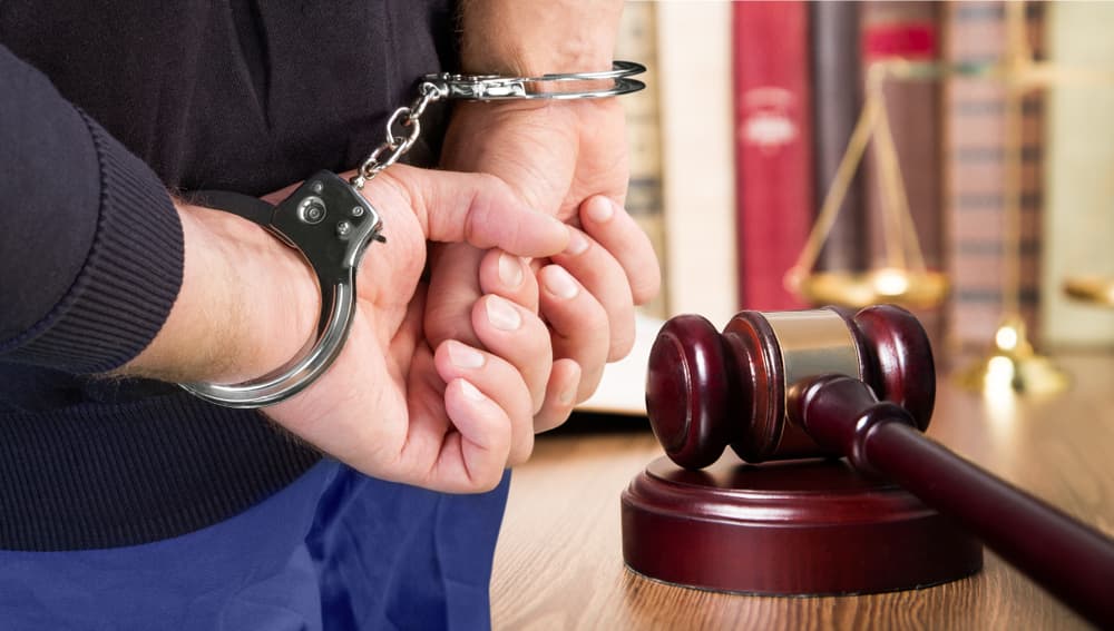 A close-up image focusing on male hands secured in handcuffs, emphasizing the theme of restraint and the legal system.