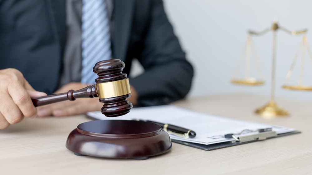 A lawyer or judge holds a gavel, preparing to preside over a case with fairness and justice. The scales of justice and legal documents are positioned nearby, symbolizing the legal process and the concept of justice. 