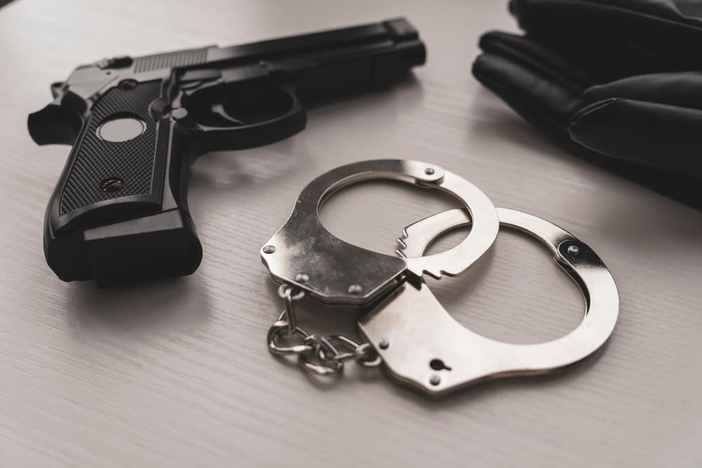 A pistol and handcuffs on a white table, representing law enforcement equipment. Firearms used by police, symbolizing the arrest and detention process.






