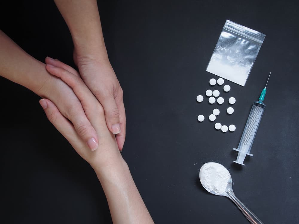 Holding hands for helping drug addict teenage on black table with drug powder, syringe and pills.