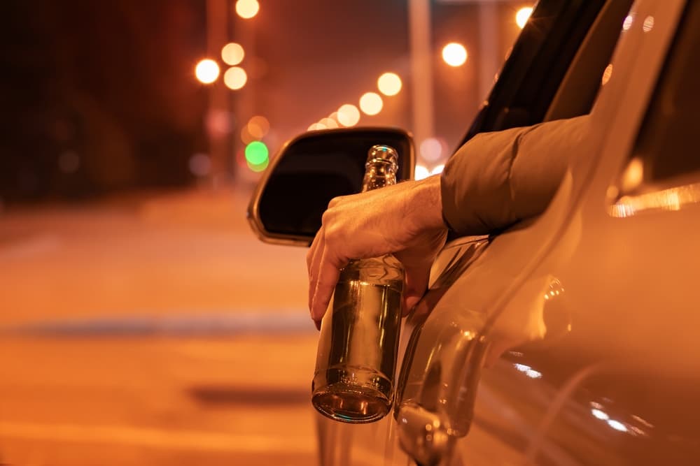 Drunk man driving a car with a bottle of beer at the night.